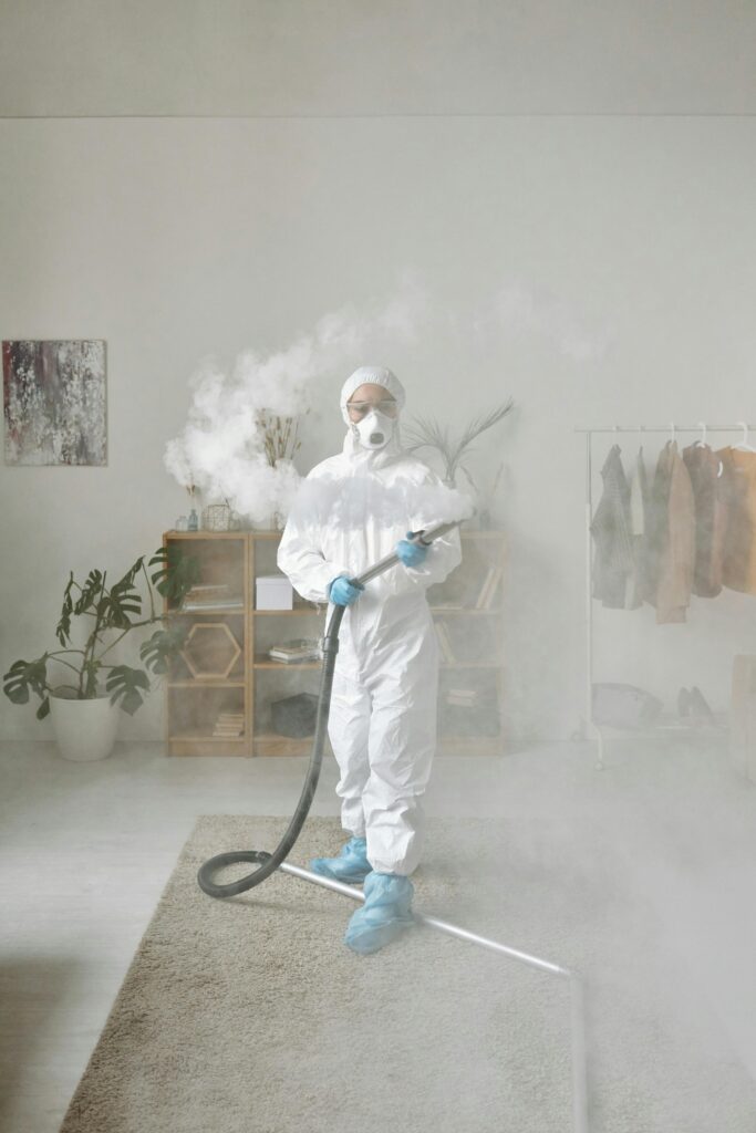 Person wearing personal protective equipment fumigating an indoor area with thick smoke.